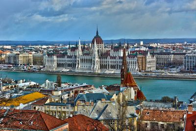 High angle view of buildings by river against cloudy sky