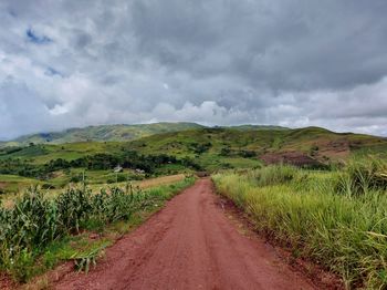 Dirt road amidst field against sky
