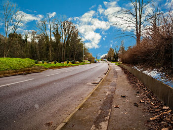 Empty road amidst trees against sky