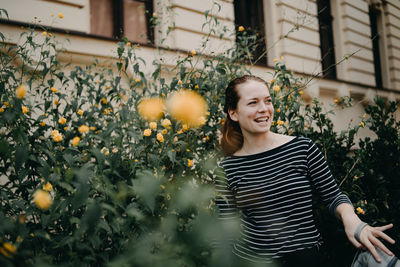 Smiling young woman standing by plants