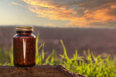 Close-up of glass jar on land by sea against sky during sunset