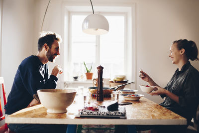 Side view of happy couple talking while eating lunch at home