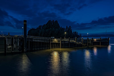 Illuminated bridge over river against sky at night