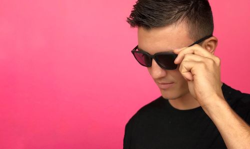 Close-up of young man wearing sunglasses against pink background