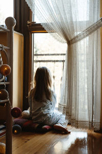 Child sitting on the floor and playing ant home. dreamy sunny mood. girl looking though the window