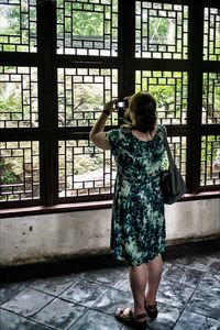 Rear view of woman photographing against window