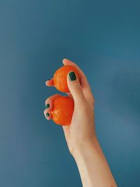 Cropped hand holding orange fruit against blue background