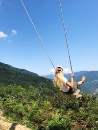 Rear view of woman sitting on swing against sky