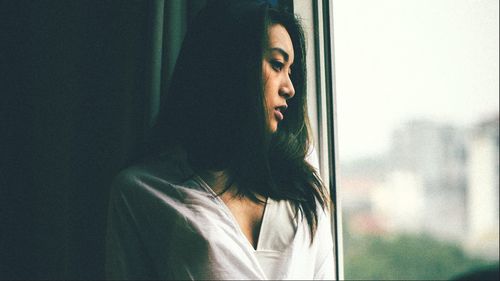 Portrait of young woman looking through window