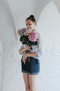 Woman holding flower standing against wall