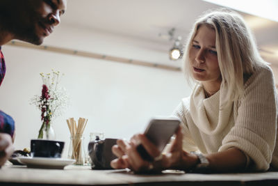 Young woman showing mobile phone to man in coffee shop