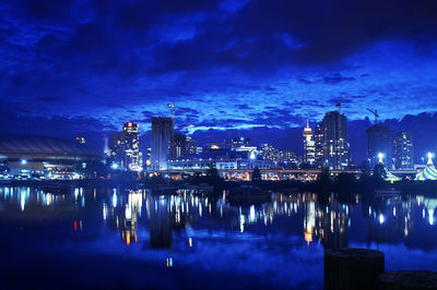 Illuminated city by sea against sky at night