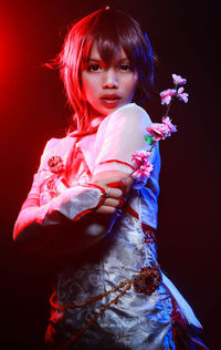 Portrait of woman with arms raised standing against black background