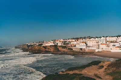 Buildings by sea against clear blue sky