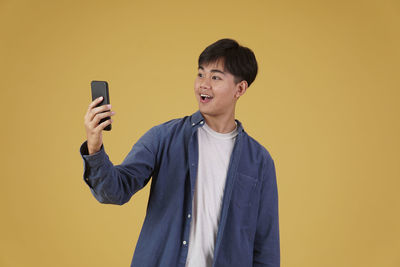 Smiling young man using mobile phone against yellow background