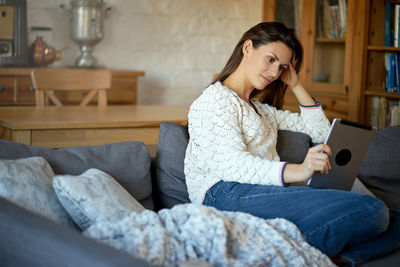 Woman using digital tablet while sitting on sofa at home