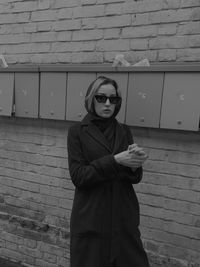 Portrait of young woman standing against brick wall