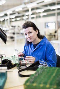 Portrait of female electrician working on circuit board at desk in industry