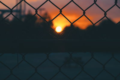 Full frame shot of chainlink fence against sky at sunset