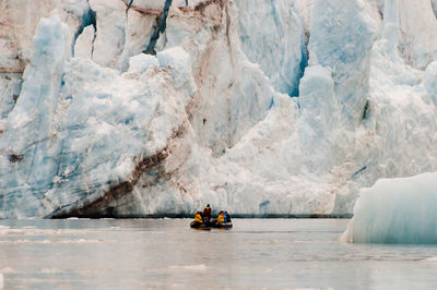 People on raft in sea against glacier