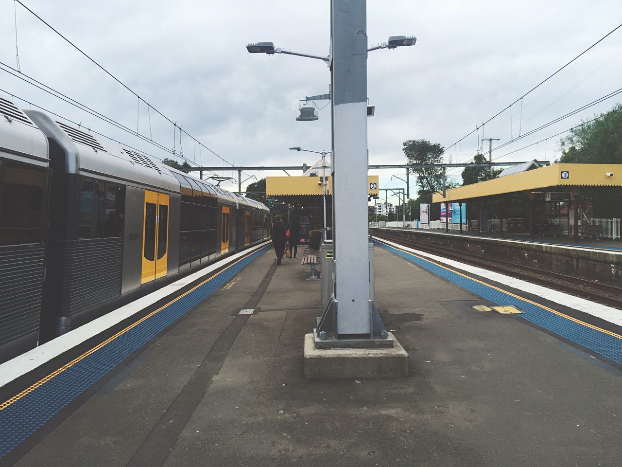 railroad track, transportation, rail transportation, public transportation, railroad station platform, railroad station, built structure, architecture, sky, building exterior, mode of transport, train - vehicle, the way forward, power line, city, diminishing perspective, cloud - sky, connection, travel, passenger train