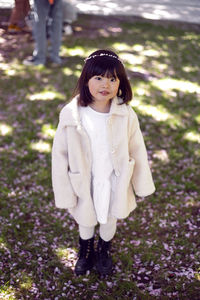 Korean girl in a white light fur coat and a headband stands in a garden with cherry blossoms