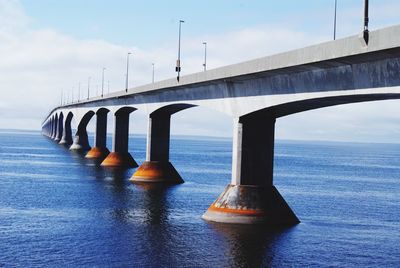 Bridge over blue sea against cloudy sky