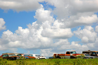 Abandoned cars on land against cloudy sky