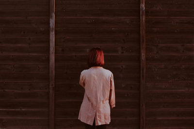 Rear view of woman standing against wooden wall