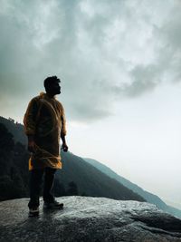 View of a man standing on a cliff against a thunderous sky 