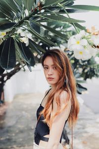 Portrait of young woman standing against tree