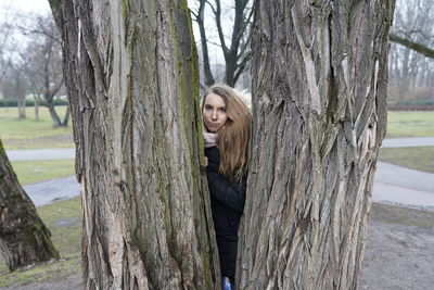 Portrait of smiling woman seen through tree trunk