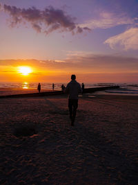 Rear view of silhouette man on beach against sky during sunset