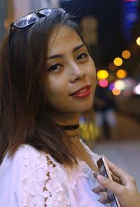 Close-up portrait of young woman using phone in city at night