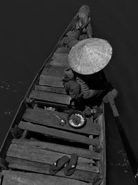 High angle view of man wearing asian style conical hat while sitting on wooden boat over river