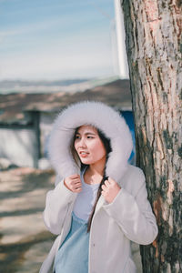 Portrait of young woman standing on tree trunk during winter