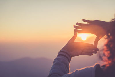 Midsection of man holding sun against sky during sunset