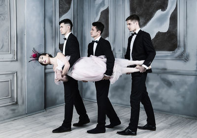 Well-dressed men carrying ballet dancer while walking on floor