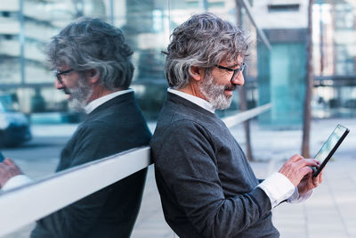 Portrait of senior man using digital tablet and browsing internet while standing against window