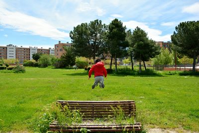Rear view of young boy jumping in the park on a bench full of plants