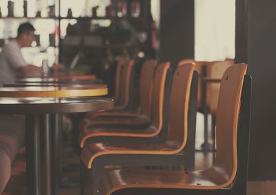 Close-up of empty chairs and table with man in background