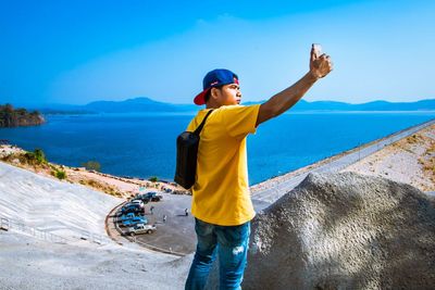 Man taking selfie on mobile phone while standing on rock against sea and sky