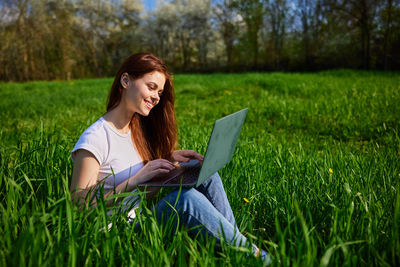 Young woman using laptop while sitting on field