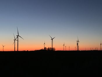 Silhouette wind turbines on field against sky during sunset