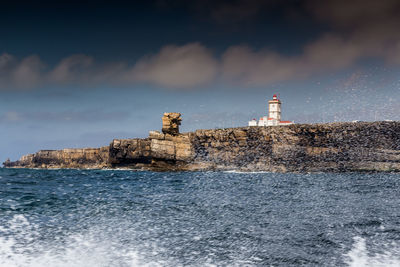 Lighthouse by sea against buildings