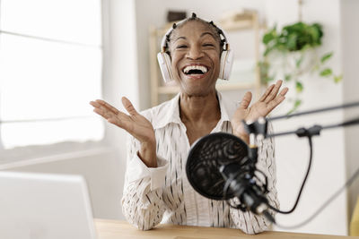 Cheerful freelancer recording podcast with microphone at home office