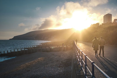 Rear view of people walking on railing by mountain against sky