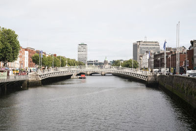 Half penny bridge over river liffey by  buildings in dublin city against sky