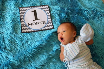 High angle view of baby boy by 1 month card on turquoise rug