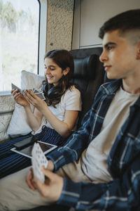 Smiling girl playing cards while sitting next to brother in train